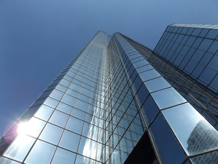 Upward view of a glass skyscraper reflecting the blue sky and sunlight, epitomizing modern urban architecture.